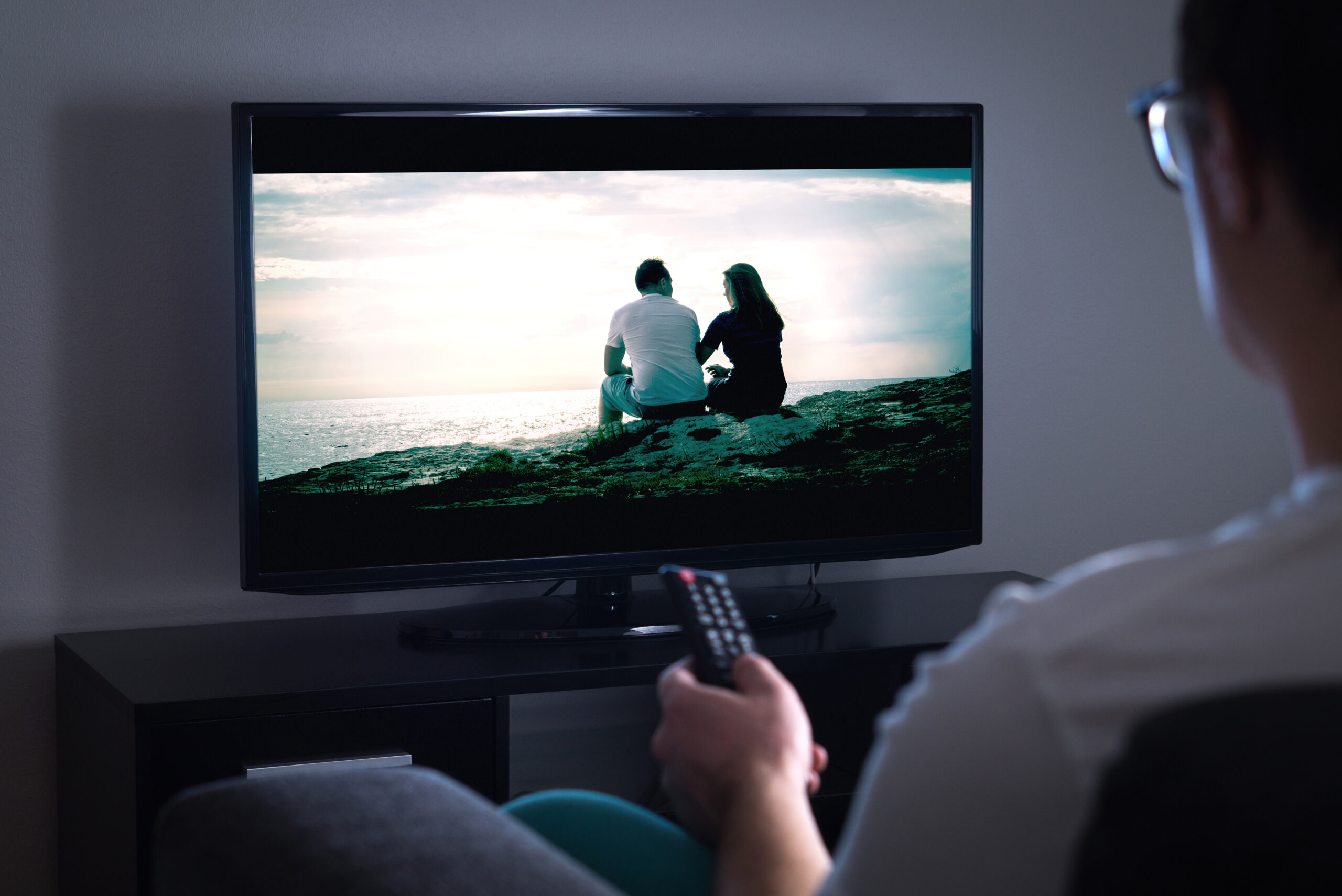 Man watching tv or streaming movie or series with smart tv at ho Man watching tv or streaming movie or series with smart tv at home. Film or show on television screen. Person holding the remote control or switching channel. Turning on or off tv.